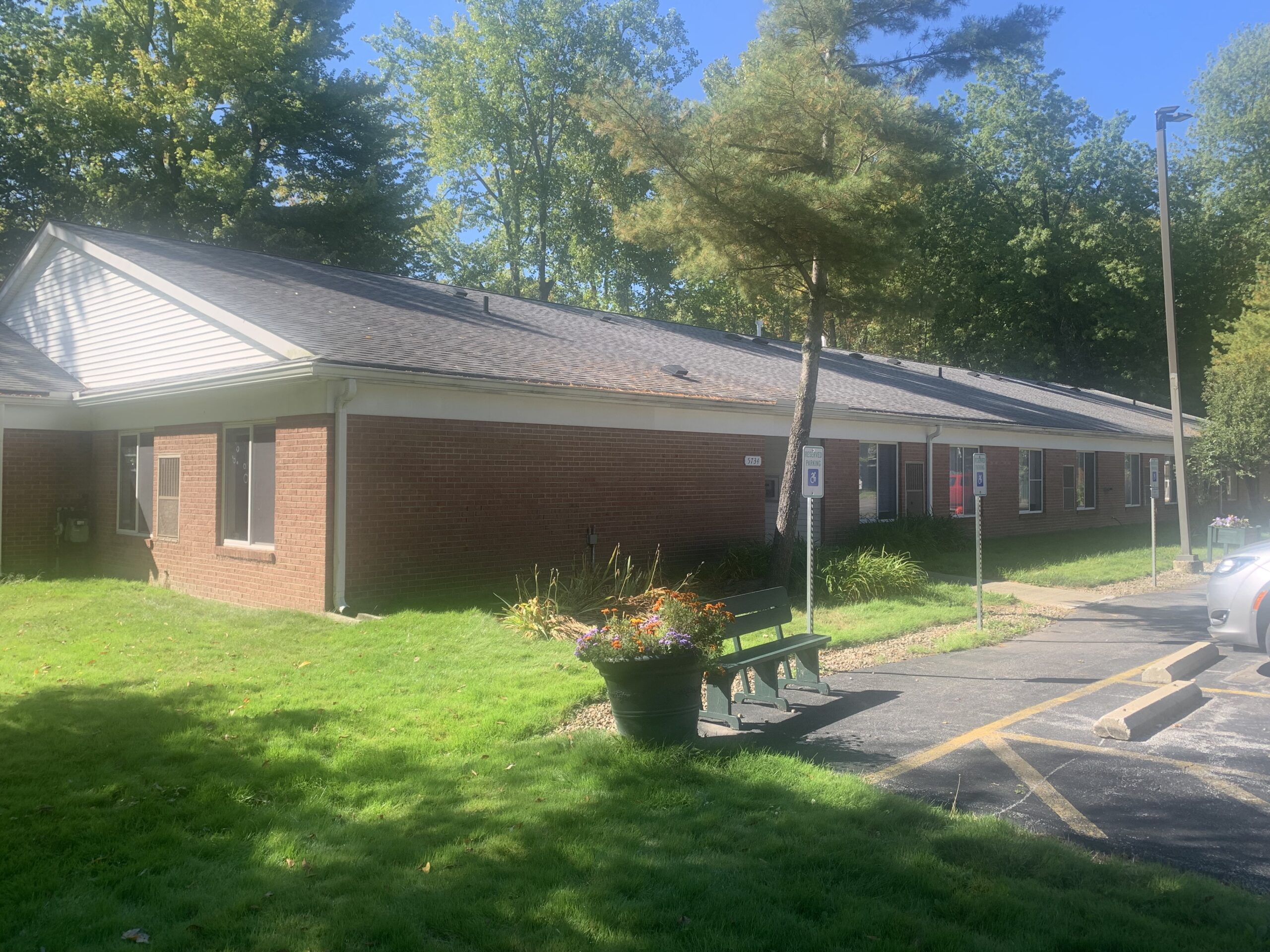 Picture of Lake Vistas building. Brick building with grey roof. Planters outside the building, lining the parking lot.