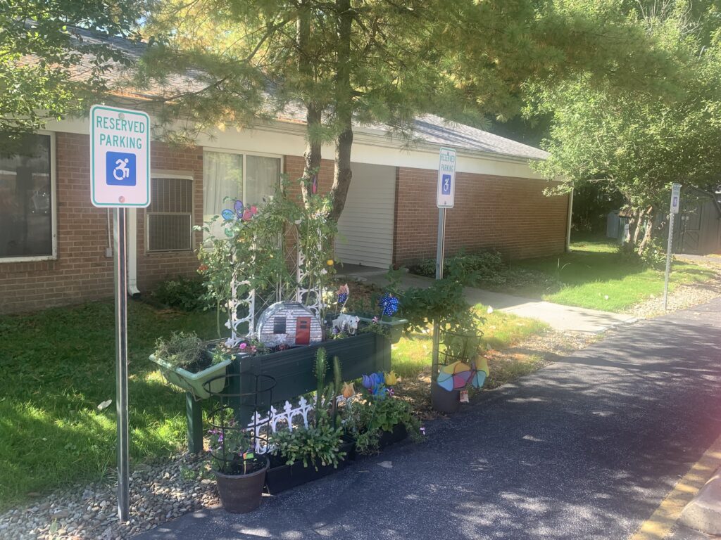 [Image] Picture of garden box filled with plants, flowers, and decorative white, picket fence.