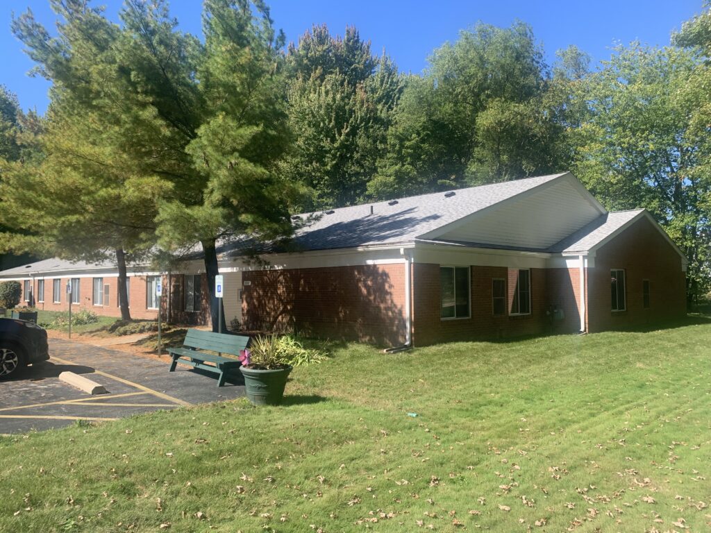 [Image] Photo of Lakes Vistas building with green bench out front, with flower pot next to bench.
