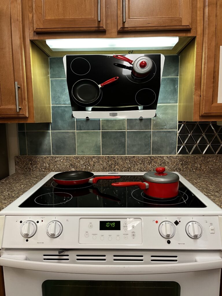 Close up picture of stove top with front controls. Mirror above range with two pans on top.