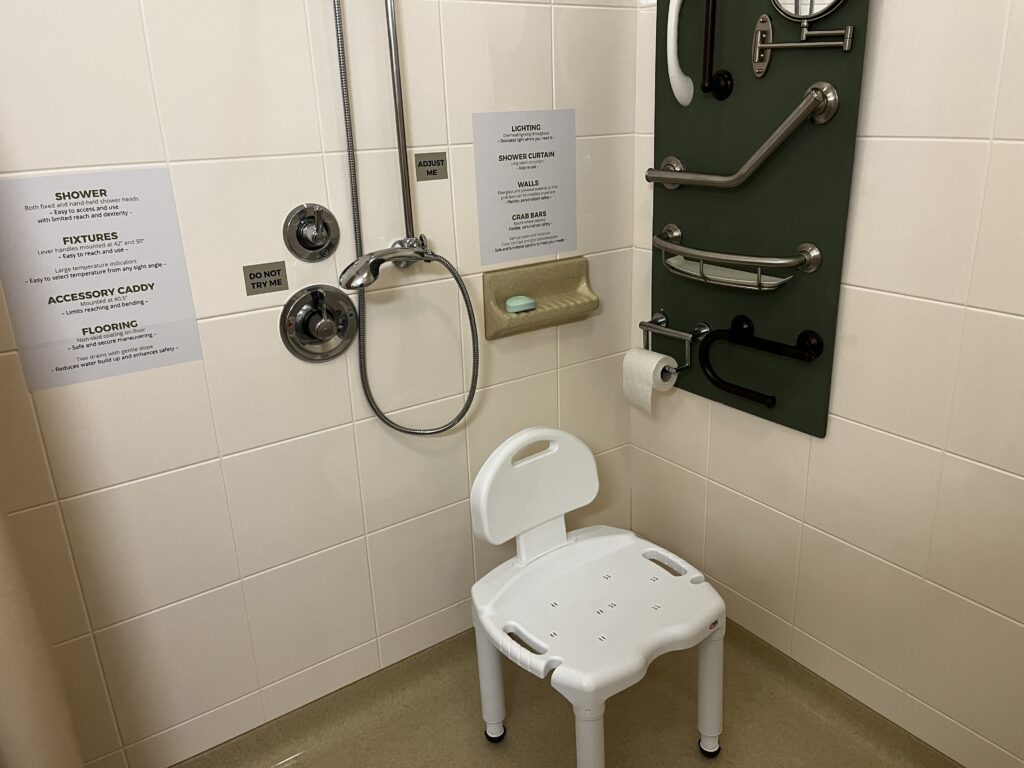 Picture of open, roll-in shower. Adjustable, removeable showerhead on back wall. Shower seat in corner.