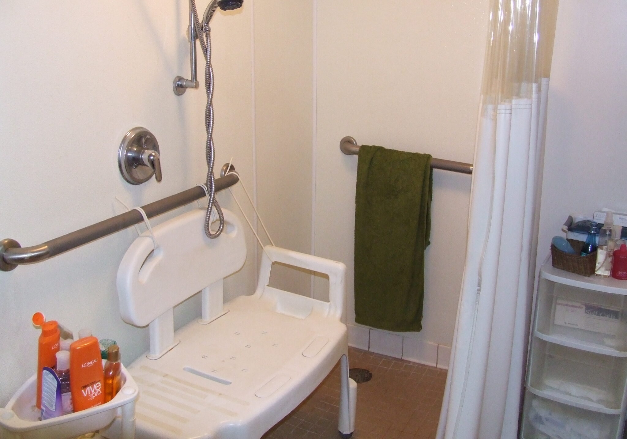 Picture of roll in shower. Adjustable showerhead on wall, two grab bars, and shower seat.